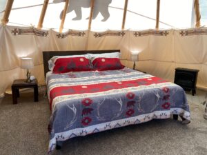 Tipi interior with king bed, end tables, and electric fireplace heater