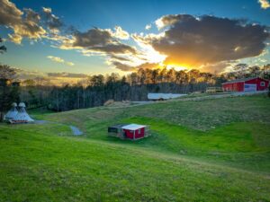 Tipis, wagons, chicken coop, and barn under a beautiful sunset